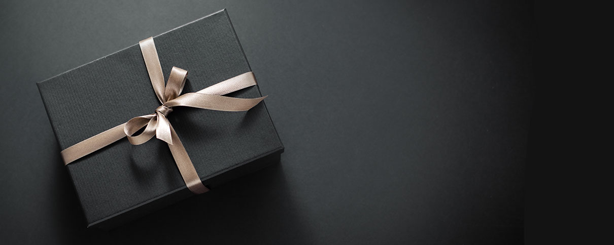 Gift wrapped in black paper and a golden bow sitting on a desk