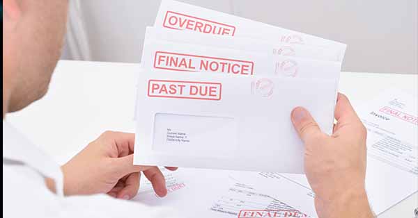 A man is holding three envelopes containing warnings of unpaid bills.